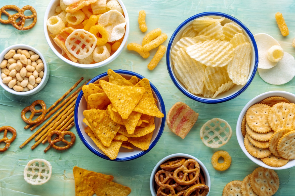 salty-snacks-party-food-on-a-blue-background-potato-and-tortilla-chips-crackers-and-other-appetizers-in-bowls-overhead-flat-lay-shot